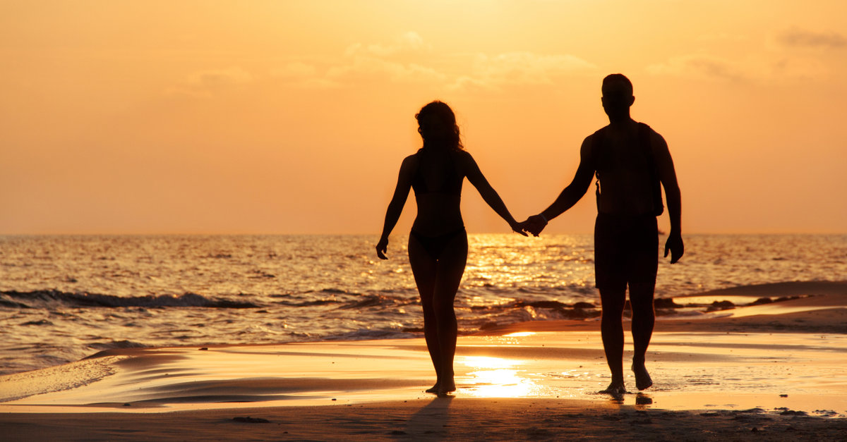 Silhouette of a couple walking at the beach in front of the suns