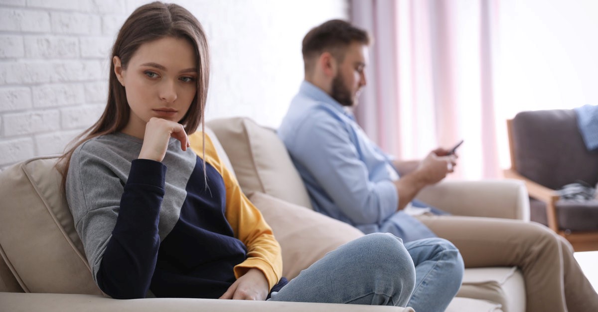 sad woman while boyfriend looking at his phone