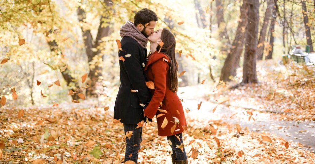 couple kissing while leaves are falling