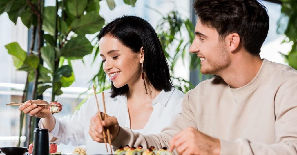 man looking at a woman while they're eating sushi