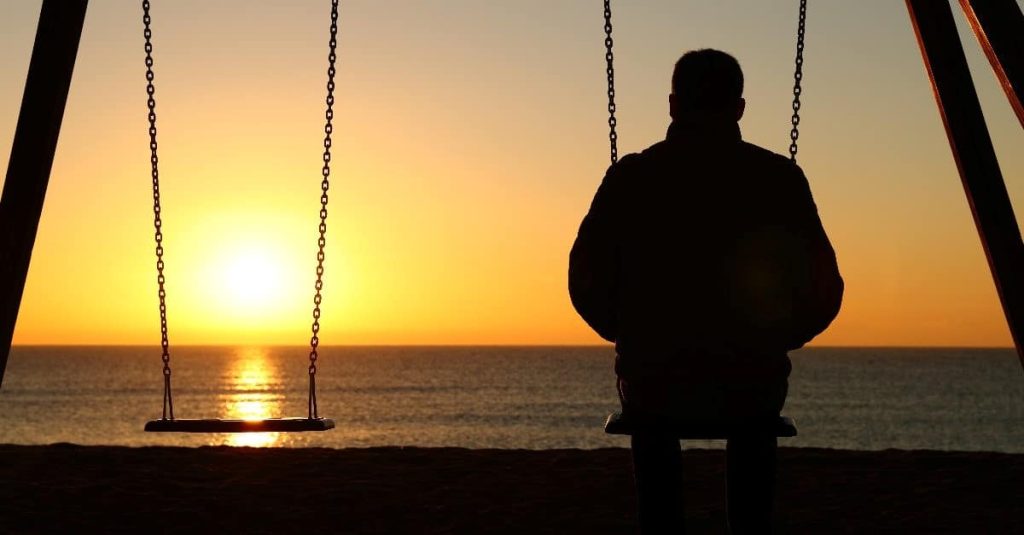 man sitting alone at a swingset