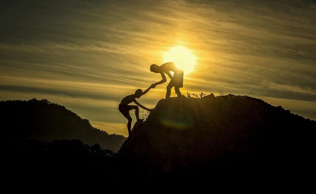 silhoutte of a man helping a boy climb a mountain