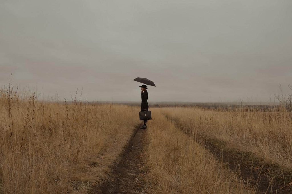 woman with suitcase and umbrella standing on a meadow