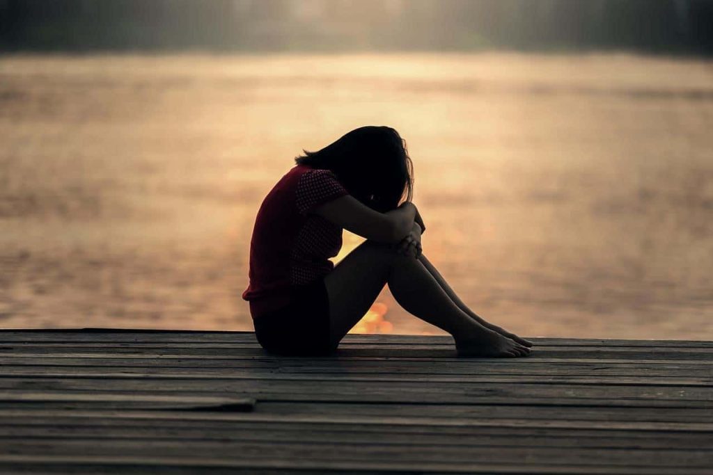 girl with head on her knees sitting on a dock