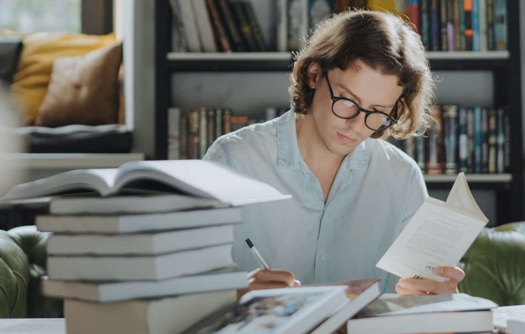 man taking notes with piles of books