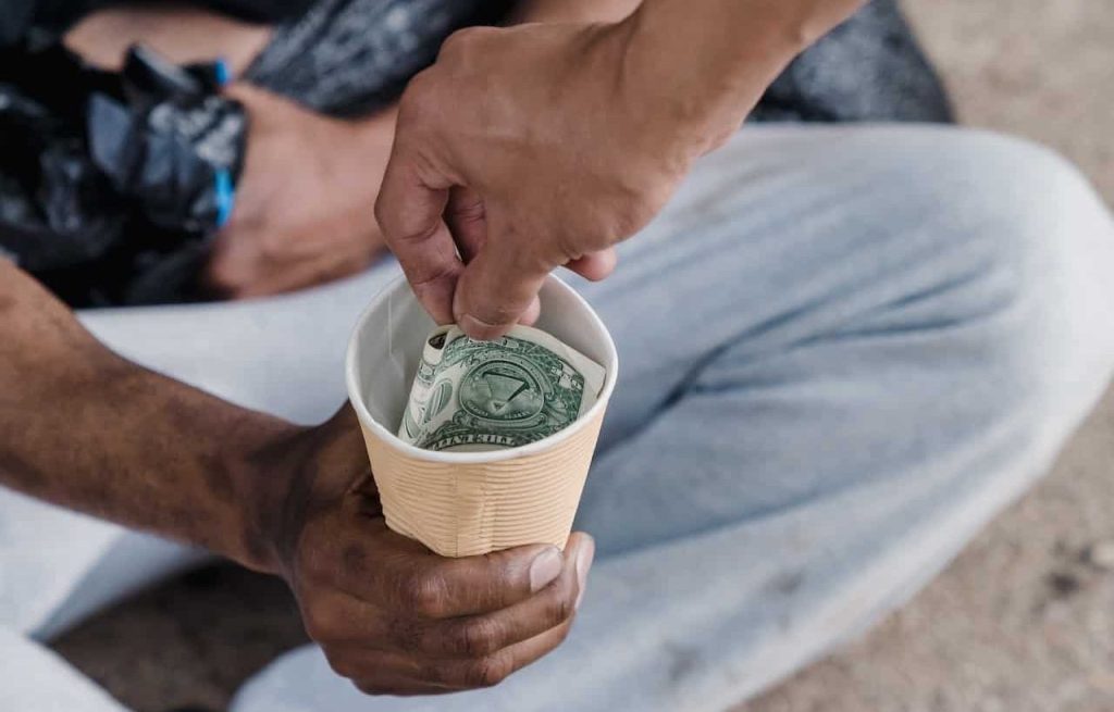 man putting money on a homeless man's cup