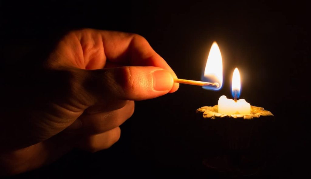 man holding a matchstick near a candle