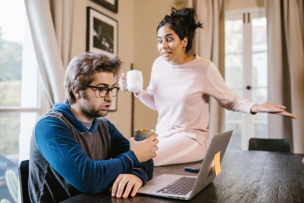 man sitting in front of laptop while woman is upset